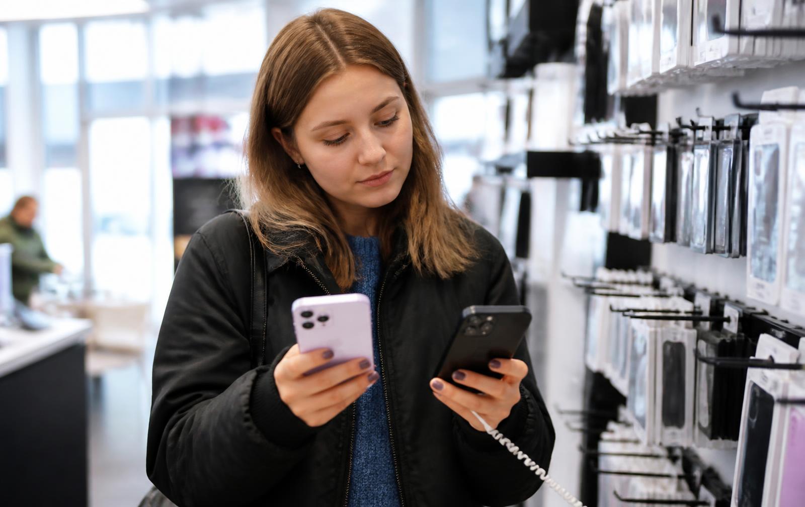 Kundin vergleicht zwei Smartphones in einem Elektronikgeschäft